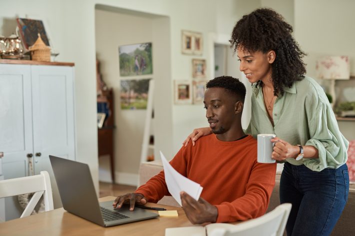 Smiling Multiracial Couple Paying Their Bills Online At Home